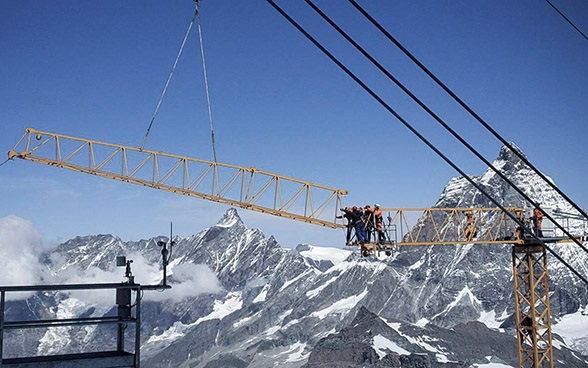 Sept personnes installent une grue pour construire un téléphérique. 